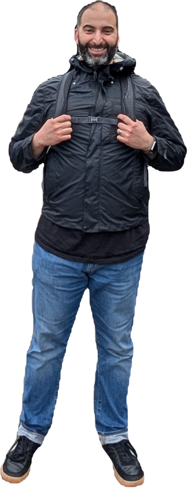 Rami standing in a black jacket and jeans, full body